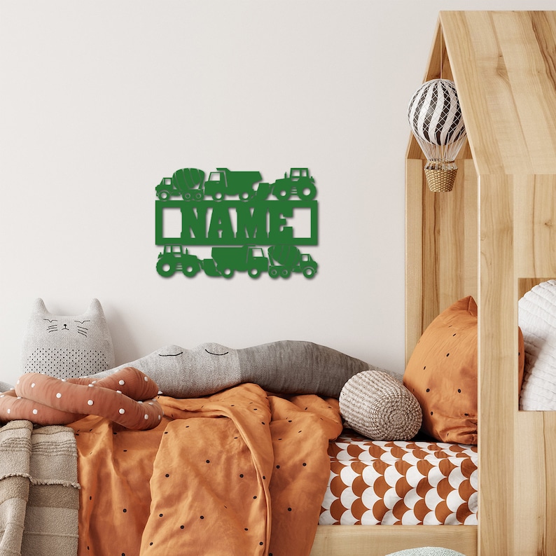 May include: Green wooden sign with a nameplate that says "NAME" surrounded by various construction vehicles, including a cement mixer, dump truck, and tractor. The sign is mounted on a white wall in a child's bedroom.