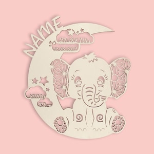 May include: A wooden cutout of an elephant sitting on a crescent moon. The elephant has detailed ears and a sweet expression. The moon has the text "NAME" and "21:35 Uhr 12.08.2019" on it. There are also clouds with the text "3120g 52cm" on them.