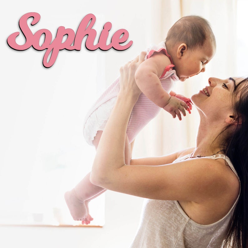 May include: A woman holding a baby girl in the air. The baby is smiling and looking up at the woman. The woman is also smiling and looking at the baby. The word "Sophie" is written in pink letters at the top of the image.