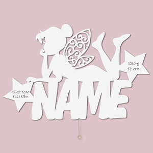 May include: White wooden cutout of a fairy with wings, lying on a star with the word "NAME" and the date "08.09.2020 13:21 Uhr" on another star. The fairy is holding a star with the text "3210 g 52 cm" on it.