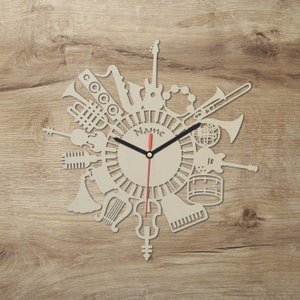 Può includere: Un orologio in legno con un quadrante circolare che presenta una varietà di strumenti musicali, tra cui una tromba, una chitarra, un violino e tamburi. Il quadrante dell'orologio ha un design in bianco e nero con la parola "Name" al centro. Le lancette dell'orologio sono nere e rosse.
