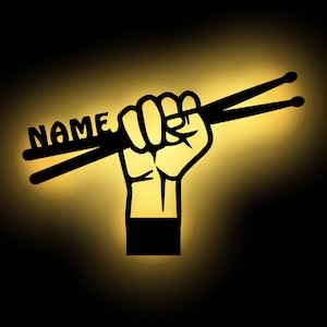 K&ouml;nnte beinhalten: Eine schwarze Silhouette einer Faust, die zwei Schlagst&ouml;cke h&auml;lt, auf denen das Wort "NAME" steht. Der Hintergrund ist ein Farbverlauf von Gelb zu Schwarz.