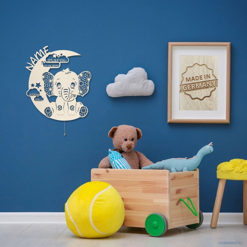 May include: A wooden toy wagon with a yellow tennis ball, a brown teddy bear, and a blue dinosaur. The wagon has green wheels and is against a blue wall with a wooden sign that says "Made in Germany".