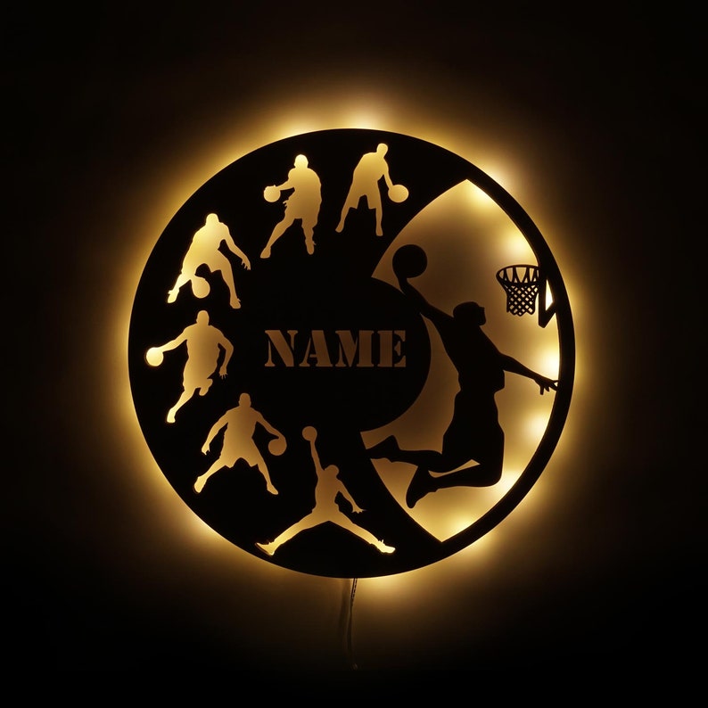 May include: Black and white silhouette of basketball players on a round wooden sign with a light behind it. The sign has the word "NAME" in the center.