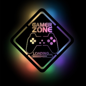Może przedstawiać: Czarny znak w kształcie rombu z białym kontrolerem do gier wideo i tekstem "GAMER ZONE LOADING..." w tęczowym gradiencie.