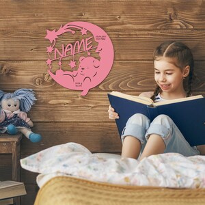 May include: Pink wooden cutout of a crescent moon with stars and a teddy bear. The moon has the text "NAME" and birth details: "22.06.2021 10:13 Uhr 2955 g 51 cm".