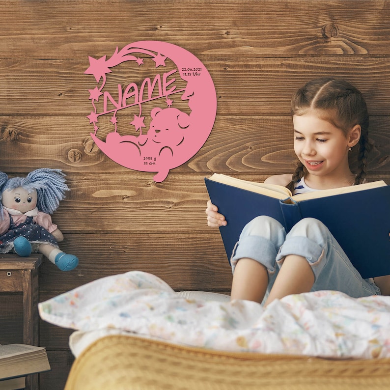 May include: Pink wooden cutout of a crescent moon with stars and a teddy bear. The moon has the text "NAME" and birth details: "22.06.2021 10:13 Uhr 2955 g 51 cm".