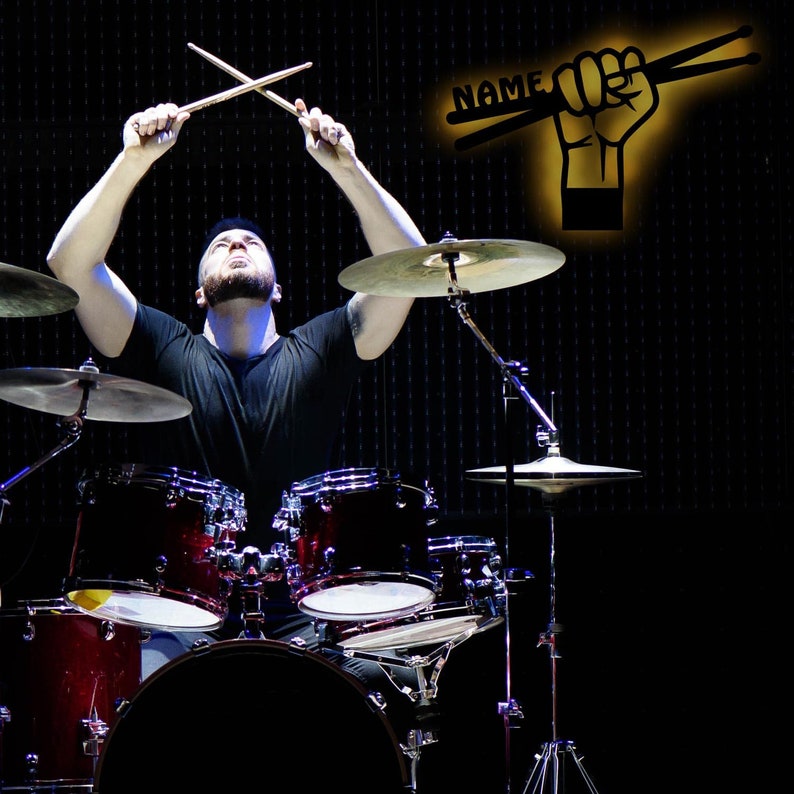 K&ouml;nnte beinhalten: Eine Person spielt ein Schlagzeug mit Drumsticks in der Luft. Die Trommeln sind rot, schwarz und silber. Die Becken sind silber. Der Hintergrund ist schwarz.