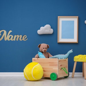 May include: A blue wall with a wooden toy wagon filled with stuffed animals, a tennis ball, and a dinosaur. The wagon has wheels and a handle. There is a yellow stool and a wooden sign that says "Name" on the wall.