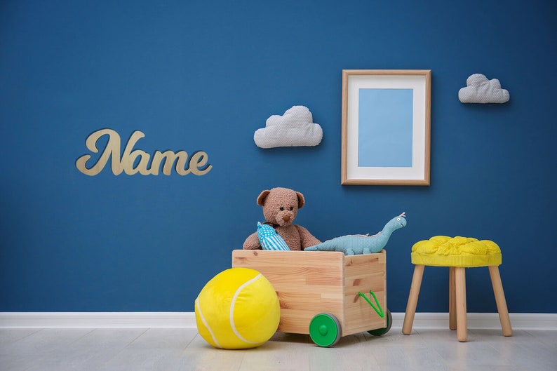 May include: A blue wall with a wooden toy wagon filled with stuffed animals, a tennis ball, and a dinosaur. The wagon has wheels and a handle. There is a yellow stool and a wooden sign that says "Name" on the wall.