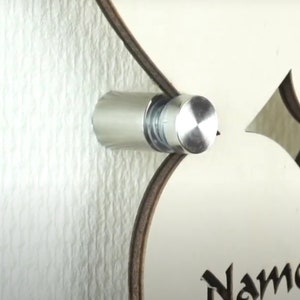 Puede incluir: Un soporte de pared de metal plateado con una tapa redonda de plata pulida. El soporte est&aacute; fijado a una pared blanca.
