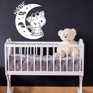 May include: White wooden crescent moon with a cute cartoon cat and stars, with a growth chart in inches and centimeters. The moon is mounted on a black wall above a white crib with a gray mattress and a white teddy bear sitting inside.