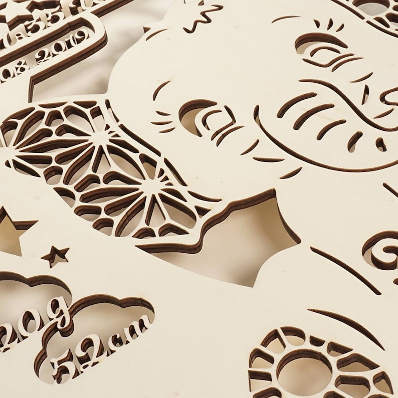 May include: A wooden cutout of an elephant with intricate details, including a floral design and the text "08.2019". The elephant is surrounded by other cutouts, including a star, clouds, and a circle with a floral design. The text "20g" and "52cm" are also visible.