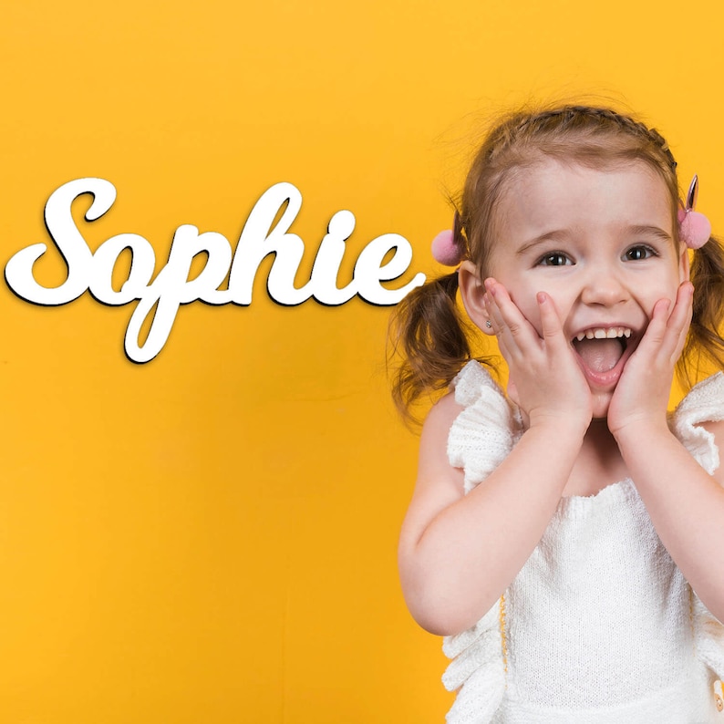 May include: A young girl with pigtails smiles excitedly in front of a yellow background with the name "Sophie" written in white cursive letters.
