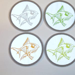 Könnte beinhalten: Vier runde Aufnäher mit weißem Hintergrund und grauem Rand. Jeder Aufnäher zeigt ein stilisiertes Haidesign in verschiedenen Farben: Grau, Grün, Orange und Limettengrün. Der Hai hat scharfe Zähne und ein skelettartiges Aussehen.