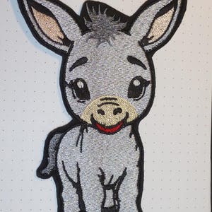 Könnte beinhalten: Gestickter Aufnäher mit einem lächelnden Esel mit großen, ausdrucksstarken Augen. Der Esel hat einen grauen Körper mit schwarzen Konturen und einer schwarzen Mähne. Die Innenohren sind beige und der Mund rot. Geeignet für Kleidung oder Accessoires.