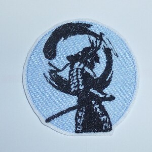 Könnte beinhalten: Runder, gestickter Aufnäher mit einem schwarzen Samurai-Krieger-Design auf hellblauem Hintergrund. Der Samurai wird mit einem Schwert in einer dynamischen Pose dargestellt. Der Aufnäher hat einen weißen Rand.