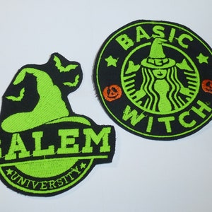 Könnte beinhalten: Zwei gestickte Aufnäher mit Halloween-Motiven. Ein Aufnäher ist schwarz mit einem grünen Hexenhut und dem Text "SALEM UNIVERSITY". Der andere Aufnäher ist schwarz mit einem grünen Hexenlogo und dem Text "BASIC WITCH".