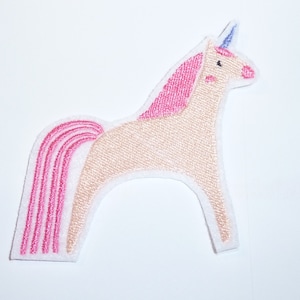 Könnte beinhalten: Ein skurriles, gesticktes Aufnäher mit einem hellbraunen Einhorn mit rosa Mähne, Schweif und Rouge. Das Einhorn hat ein blaues Horn und ist weiß umrandet. Dieser Aufnäher eignet sich für Kleidung, Taschen oder andere Stoffartikel.