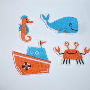 Könnte beinhalten: Set aus vier aufgestickten Aufnähern mit Meeresbewohnern. Enthält ein orangefarbenes Seepferdchen, einen blauen Wal, ein orangefarbenes Boot mit blauer Kabine und eine orangefarbene Krabbe. Nautisches Thema.