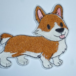 Könnte beinhalten: Gestickter Aufnäher mit einem lächelnden Corgi-Hund mit braun-weißem Fell, schwarzen Augen und einer rosa Zunge. Der Aufnäher hat eine schwarze Umrandung und ist zum Aufbügeln oder Aufnähen auf Stoff vorgesehen. Der Corgi ist in einem verspielten Cartoon-Stil dargestellt.