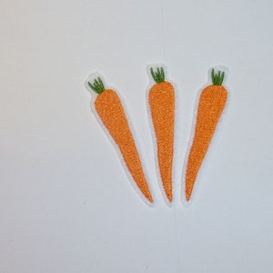 Könnte beinhalten: Drei orangefarbene Karottenaufnäher mit grünen Spitzen und weißen Rändern vor weißem Hintergrund. Die Aufnäher sind mit einem strukturierten Aussehen bestickt und zeigen eine leuchtende orange Farbe.