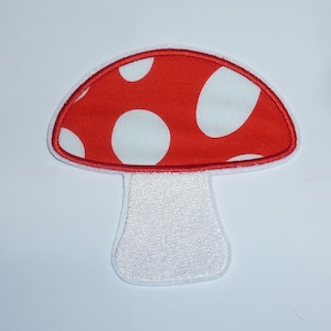 Könnte beinhalten: Ein rot-weißer Pilzaufnäher mit weißem Stiel. Der Pilzhut ist rot mit weißen Tupfen und einem roten Rand. Der Stiel ist weiß mit strukturiertem Aussehen.