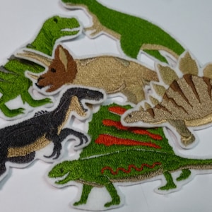 Könnte beinhalten: Gestickte Dinosaurier-Patches in Grün, Gold, Braun und Schwarz. Die Patches zeigen verschiedene Dinosaurierarten mit detaillierten Nähten und weißen Rändern. Ideal zum Aufnähen auf Kleidung oder Accessoires.
