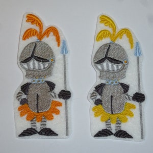 Könnte beinhalten: Zwei aufgestickte Ritteraufnäher. Jeder Ritter trägt einen silbernen Helm mit gelber Feder, eine silberne Rüstung und einen gelb-orangen Rock. Sie halten einen blauen Speer und haben einen blauen Kragen.