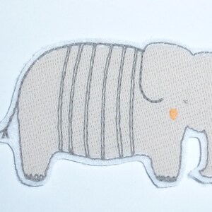 Könnte beinhalten: Ein hellbeige Elefantenaufnäher mit grauen vertikalen Streifen und einer grauen Umrandung. Der Elefant hat einen kleinen orangefarbenen Punkt als Auge und ist ein niedliches, skurriles Design. Dieser Aufnäher eignet sich für Kinderkleidung oder Accessoires.