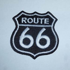 Könnte beinhalten: Gestickter Route 66-Aufnäher in Schwarz und Weiß. Der Aufnäher hat die Form eines Schildes mit dem Wort „ROUTE“ über der Zahl „66“. Text und Rand sind weiß auf schwarzem Hintergrund.