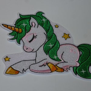Könnte beinhalten: Gestickter Aufnäher eines schlafenden Einhorns mit weißem Körper, grüner Mähne und Schweif sowie einem goldenen Horn. Das Einhorn hat geschlossene Augen und ist von gelben Sternen umgeben. Der Aufnäher hat einen weißen Rand.