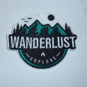Könnte beinhalten: Gestickter Aufnäher mit Berg- und Waldmotiv. Der Aufnäher zeigt das Wort "WANDERLUST" in weißen Buchstaben mit "EXPLORE" darunter. Die Berge sind türkis, und der Aufnäher hat ein Schwarz-Weiß-Farbschema.