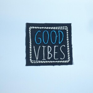 Könnte beinhalten: Ein quadratischer, marineblauer, gestickter Aufnäher mit den Worten "GOOD VIBES" in blauem und weißem Faden. Der Text befindet sich innerhalb eines weißen, gestickten Rahmens. Der Aufnäher befindet sich auf weißem Hintergrund.