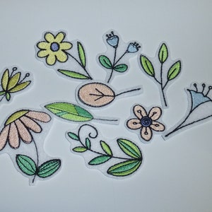 Könnte beinhalten: Eine Sammlung gestickter Blumenaufnäher in verschiedenen Designs. Die Aufnäher zeigen Blumen und Blätter in Pastellfarben wie Gelb, Rosa und Blau, mit grünen Stielen und schwarzen Nähten. Die Aufnäher befinden sich auf weißem Hintergrund.