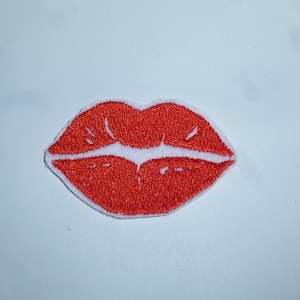 Könnte beinhalten: Gestickter Aufnäher mit roten Lippen und weißer Kontur. Die Lippen sind leuchtend rot und haben eine strukturierte Optik. Der Aufnäher ist zum Aufbügeln oder Aufnähen auf Kleidung oder Accessoires gedacht.