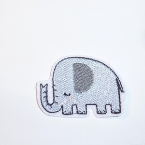 Könnte beinhalten: Hellblauer Elefantenaufnäher mit grauem Ohr und weißem Rand. Der Elefant hat einen kleinen Rüssel und lächelt. Der Aufnäher ist aus Stoff und eignet sich für Kleidung oder Accessoires.
