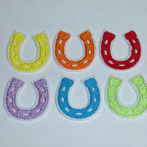 Könnte beinhalten: Sechs gestickte Hufeisen-Aufnäher in den Farben Gelb, Orange, Rot, Lila, Blau und Grün. Jedes Hufeisen hat einen weißen Rand und ist vor einem weißen Hintergrund platziert. Ideal für Bastelarbeiten.