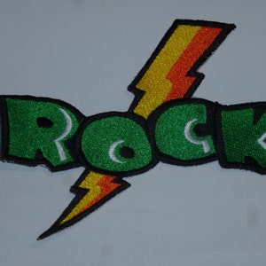 Könnte beinhalten: Gestickter Aufnäher mit dem Wort "ROCK" in grünen Buchstaben, schwarz umrandet. Ein gelber, orangefarbener und roter Blitz befindet sich hinter dem Wort. Geeignet für Kleidung oder Accessoires.
