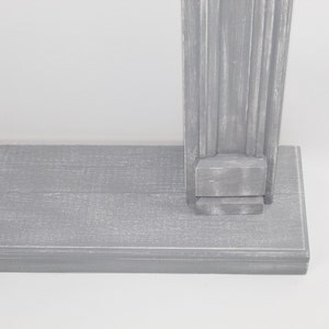 K&ouml;nnte beinhalten: Ein graues Holzregal mit einer dekorativen, geriffelten S&auml;ule auf der rechten Seite. Das Regal besteht aus Holzbrettern und hat einen abgenutzten, verwitterten Look.