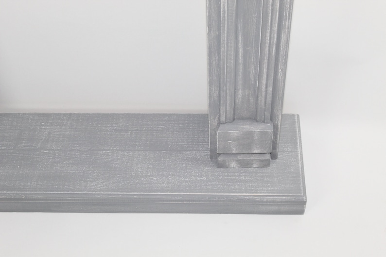 K&ouml;nnte beinhalten: Ein graues Holzregal mit einer dekorativen, geriffelten S&auml;ule auf der rechten Seite. Das Regal besteht aus Holzbrettern und hat einen abgenutzten, verwitterten Look.