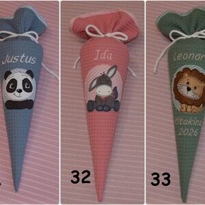 May include: Three cone-shaped fabric gift bags with waffle texture, drawstring closures, and gingham trim. The blue bag features a panda and the name Justus. The pink bag features a donkey and the name Ida. The green bag features a lion and the name Leonard.