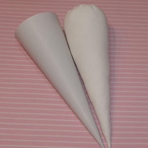 May include: Two white cone-shaped objects positioned side by side. The left object has a smooth, rigid surface with a wide circular opening at the top. The right object appears to be a fabric-covered cone with a rounded, gathered top closure.