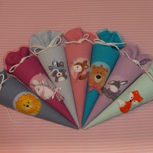 May include: A collection of seven cone-shaped fabric gift bags, each featuring a unique animal appliqu&eacute; including a lion, unicorn, raccoon, deer, bear, donkey, and fox. The bags are made of textured waffle fabric in various colors with white drawstring closures.