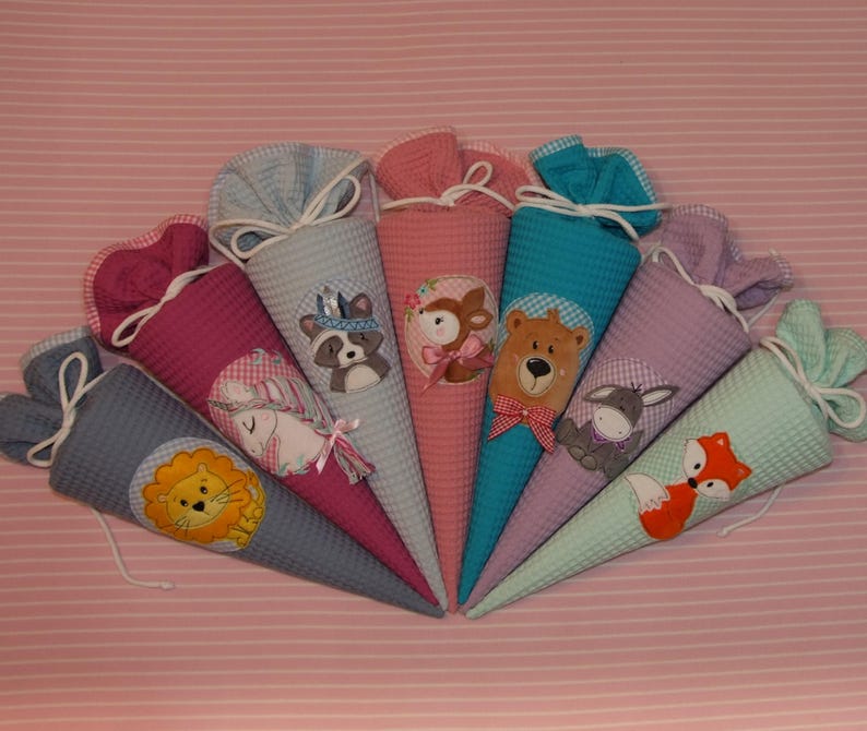 May include: A collection of seven cone-shaped fabric gift bags, each featuring a unique animal appliqu&eacute; including a lion, unicorn, raccoon, deer, bear, donkey, and fox. The bags are made of textured waffle fabric in various colors with white drawstring closures.