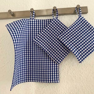 Könnte beinhalten: Ein Set aus drei blau-weiß karierten Küchentüchern, die an einer Metallstange hängen. Das Set beinhaltet ein Geschirrtuch und zwei Topflappen. Das Karomuster ist ein klassisches Gingham-Design.