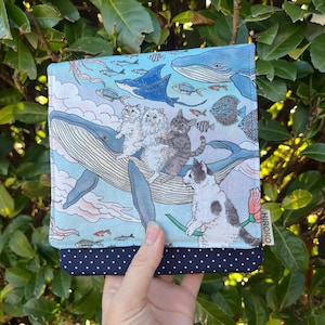 Könnte beinhalten: Eine quadratische Stofftasche mit einem hellblauen Aufdruck von Walen, Rochen, verschiedenen Fischen und drei Katzen. Der untere Teil ist dunkelblau mit weißen Punkten. Ein kleines weißes Etikett mit dem Text HIROKO ist seitlich angebracht.