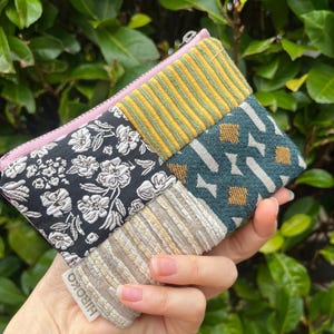 May include: A multi-fabric patchwork pouch with a pink zip. The pouch features a variety of patterns, including black floral, yellow striped, teal geometric, and beige striped designs. The brand name "HIROKO" is visible on a small tag.