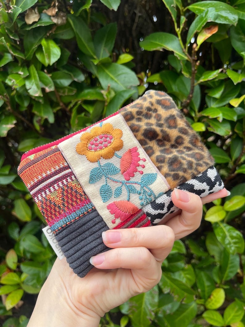 May include: A multi-textured clutch bag with a floral embroidered panel featuring a yellow and pink flower, a leopard print section, and a black and white patterned section. The bag has a ribbed grey section.