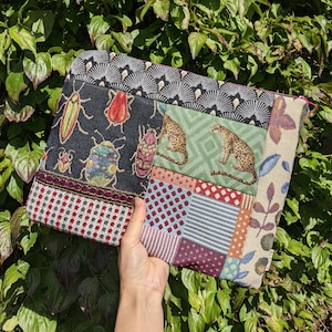 Könnte beinhalten: Eine bunte Patchwork-Clutch mit einem schwarz-weißen Insektenmuster, einem grün-weißen Tierdruck und einem rot-weiß-blauen geometrischen Muster.